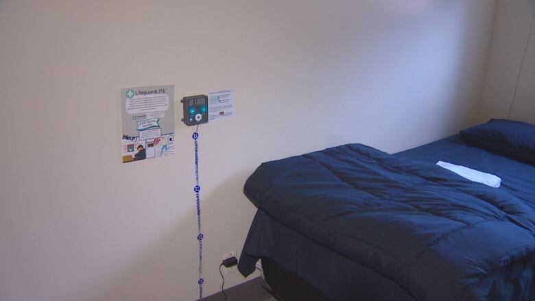 A box mounted on the wall next to a plain blue bed with a blanket in it.