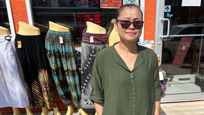 Woman in green dress and sunglasses poses for a photo in front of a storefront.