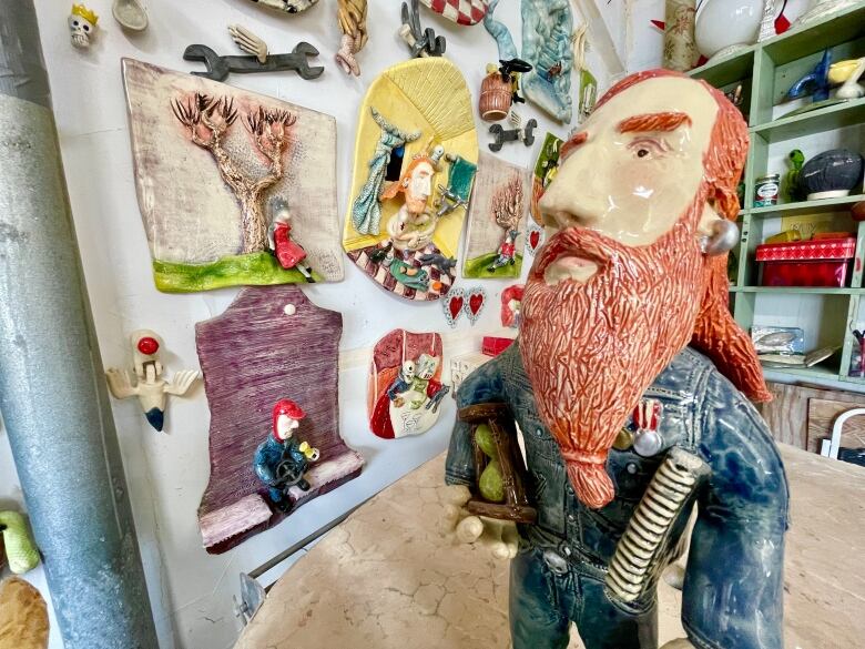 A wall of ceramic art and a sculpture of a bearded man in the foreground