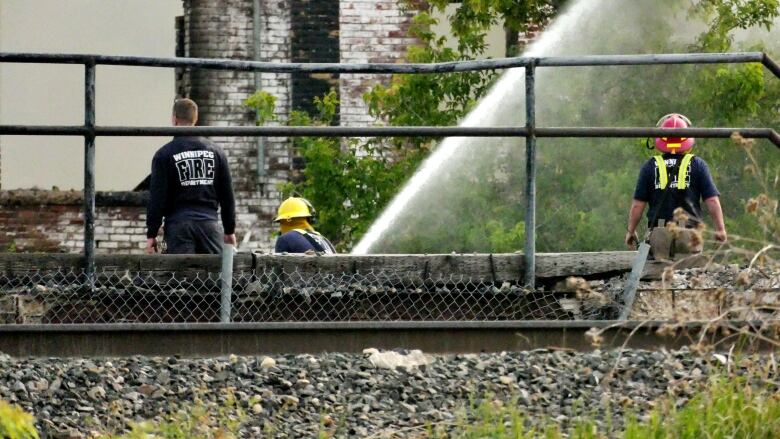 Three firefighters work on dousing a fire in an industrial building