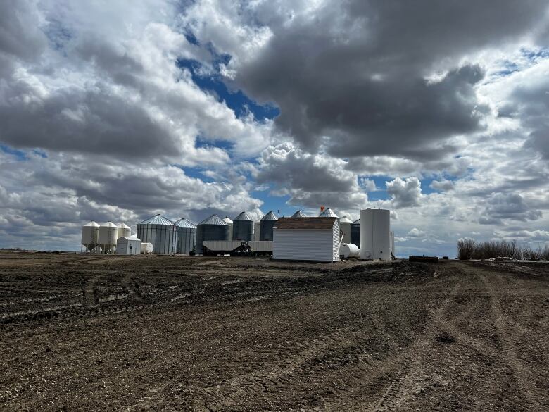 A farm can be seen with grain elevators and a cloudy sky above it. 