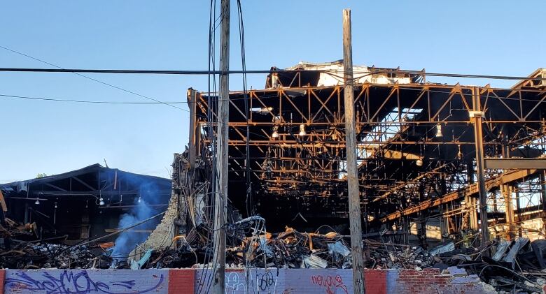 Smoke rises from the rubble of a building that burned down. The photo shows the steel frame of the building surrounded by the brick rubble.