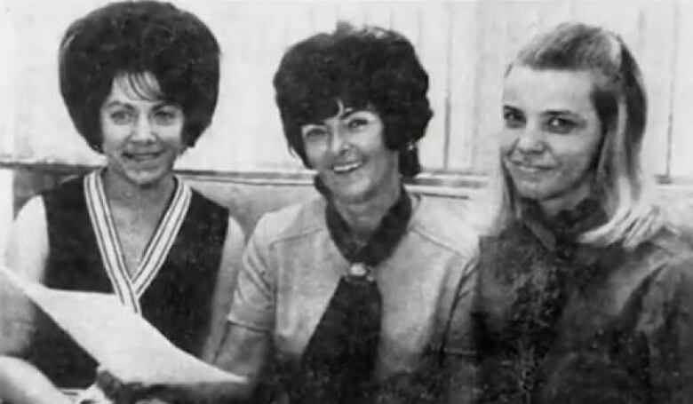 A newspaper clipping showing three women sitting down and smiling at the camera. 