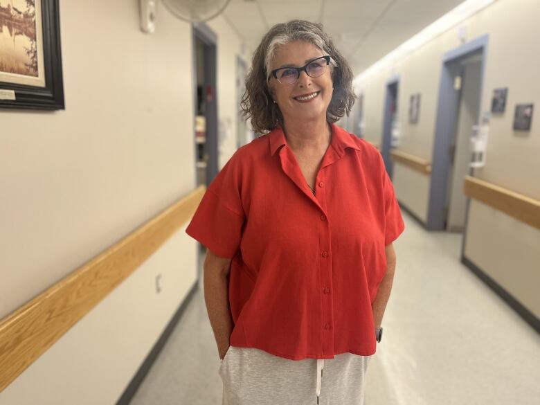 A nurse in a red shirt stands in the centre of a long hallway. 