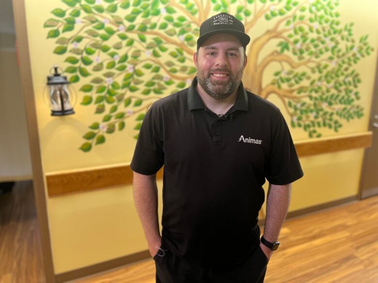 Man in a black shirt and baseball cap stands in the hospital palliative care wing.