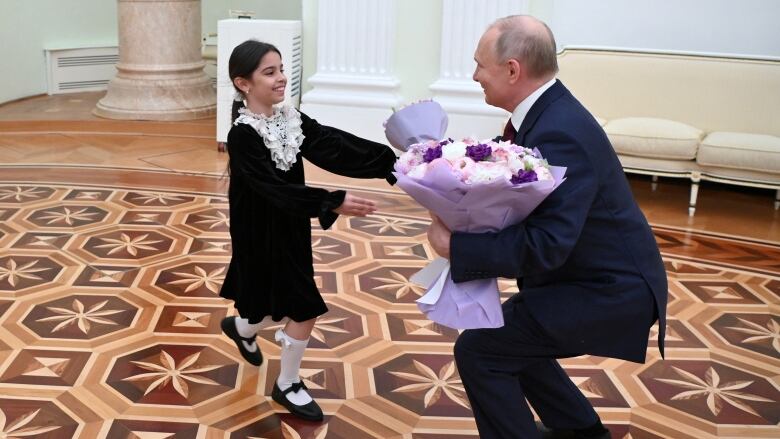 A child is greeted by an adult kneeling down and holding flowers.