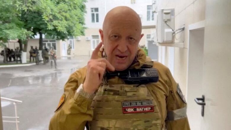 A man in military fatigues is shown speaking to a camera while outdoors.