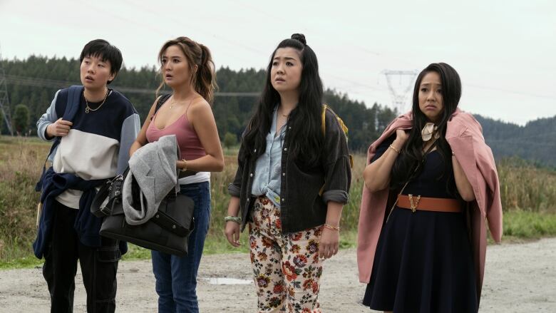 Four women stand on a dirt road. All appear disheveled and confused. 