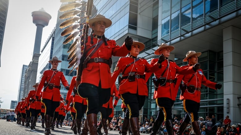 members of the RCMP in their fancy red dress uniforms march in a parade formation on a downtown Calgary street with the Calgary tower visible behind them.