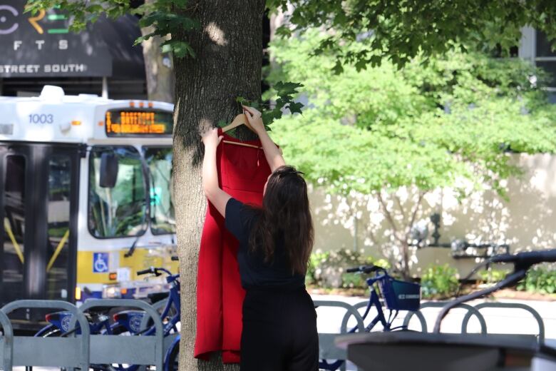 A woman hangs up a red dress. 