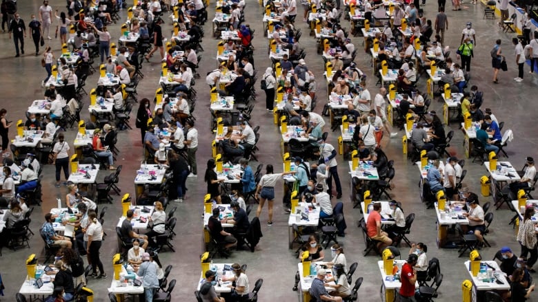 People sit at tables in an arena waiting to be vaccinated.