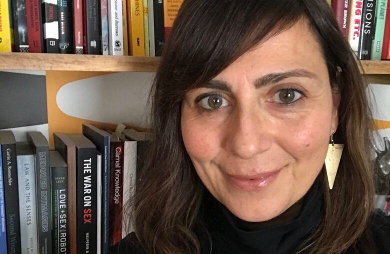 A woman posing for a photo, in front of a book shelf.