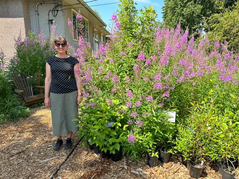 A woman stands near some tall pink flowers. 