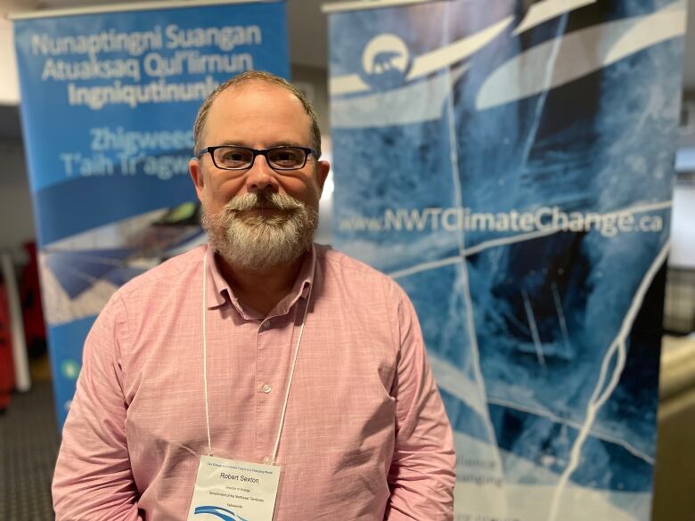 Man in pink shirt stands in front of poster of ice road.