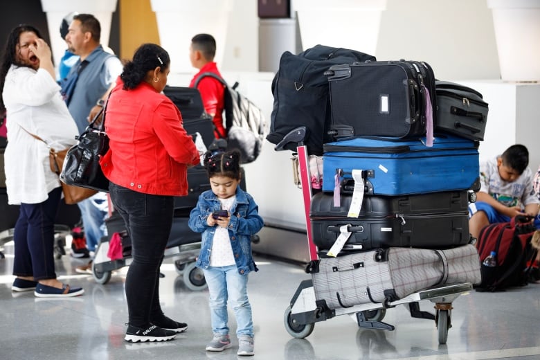 A young girl uses a cellphone while waiting in an airport.