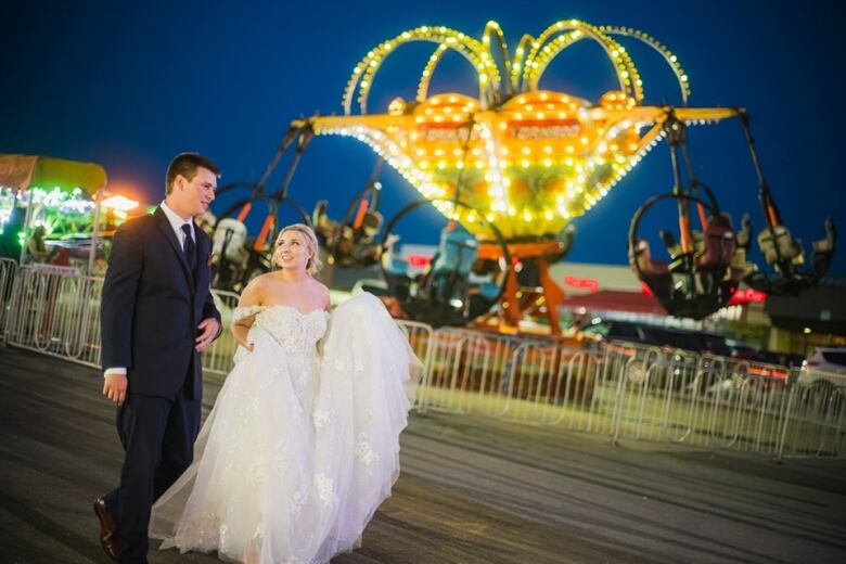 A groom and bride walking near amusement park rides. 