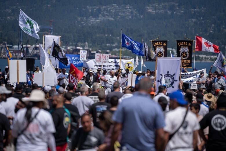 A crowd of people looks towards other people holding up blue and yellow flags at the waterfront.