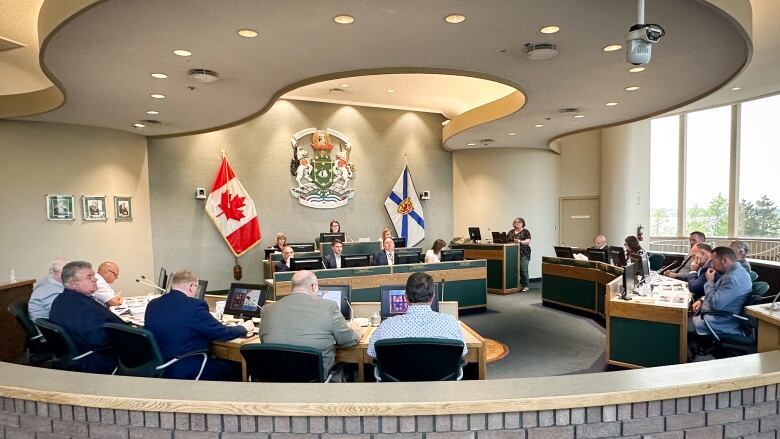 Council chamber is shown with semi-circular array of people sitting at microphones, with the Canadian and Nova Scotian flags behind.