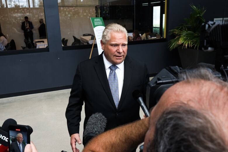 Ontario Premier Doug Ford speaks with reporters. He is wearing a black suit and blue tie.