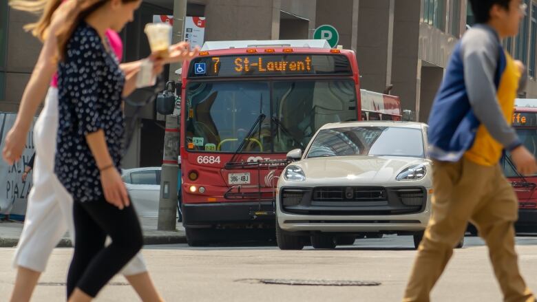 A bus waits at a red light as people cross the street in front of it.