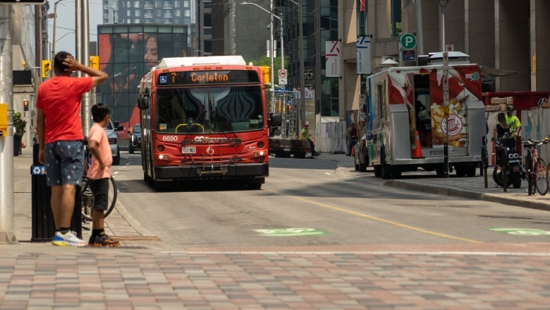 A bus approaches an intersection as people wait to cross the street.