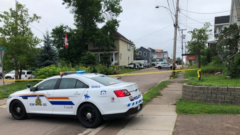 Police cars parked along a residential street with yellow crime scene tape across the road. 