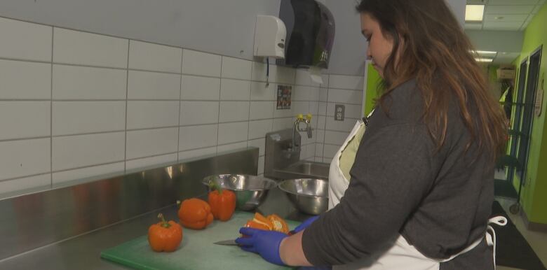 A woman with her face away from the camera chops a bell pepper. 