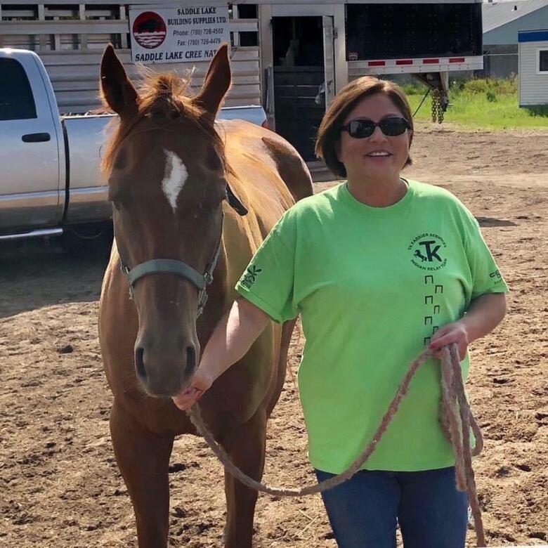 Tonya Crowchild wears a neon green team TK shirt while standing next to a brown horse.