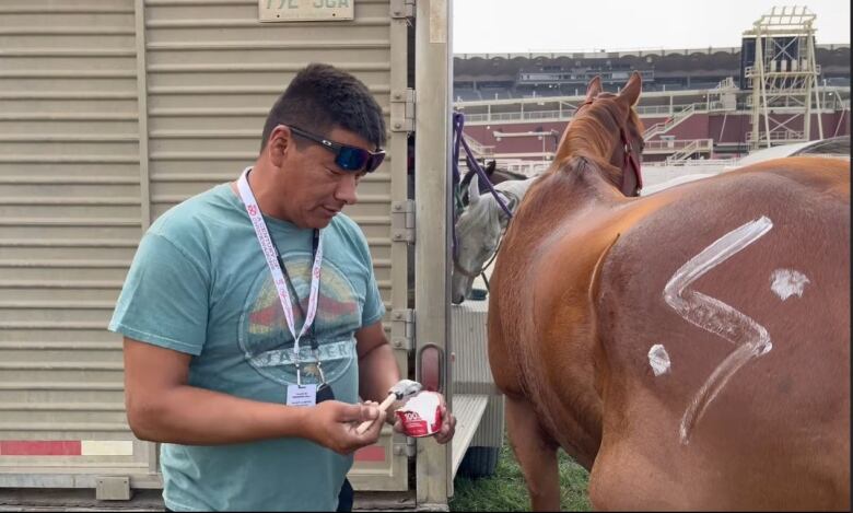 Tyson Head paints two white dots and a zigzagged line onto a brown horse.