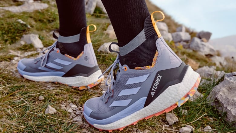 a close up shot of two feet wearing grey runners with three grey stripes and black socks walking on a grassy path.