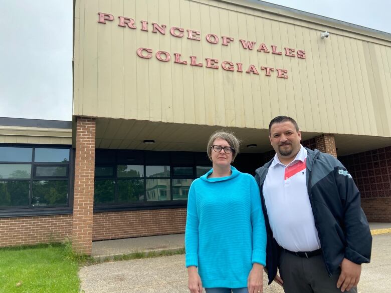 Two expressionless-looking parents stand out side a high school.