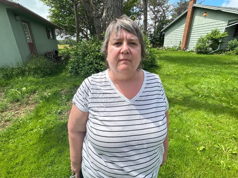 A woman with grey hair and a striped t-shirt stands in her backyard. 