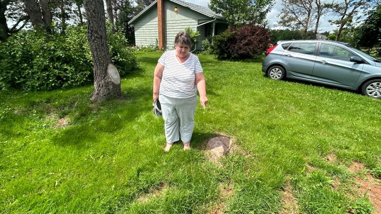 A woman stands in a grassy backyard pointing at a stump. 