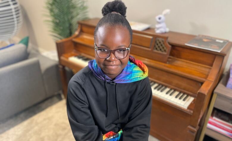 A young girl smiles at the camera as she sits in front of an apartment-size piano.