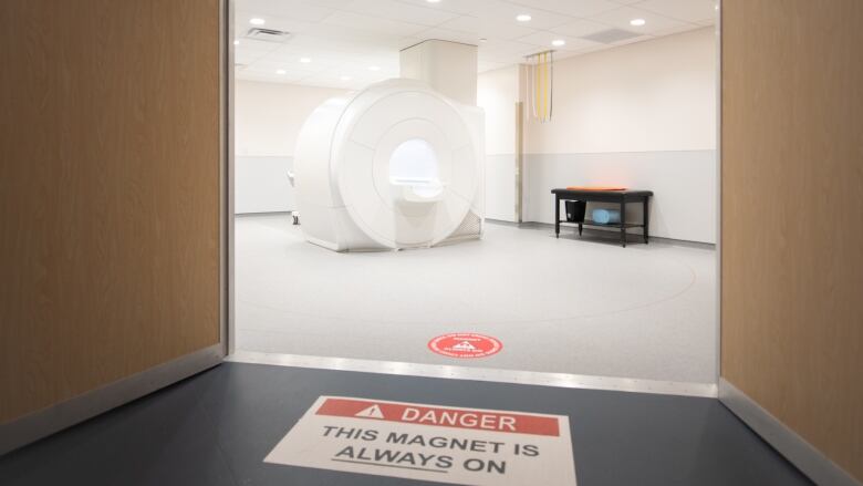 View of MRI machine through doors, with warning sign on the floor.