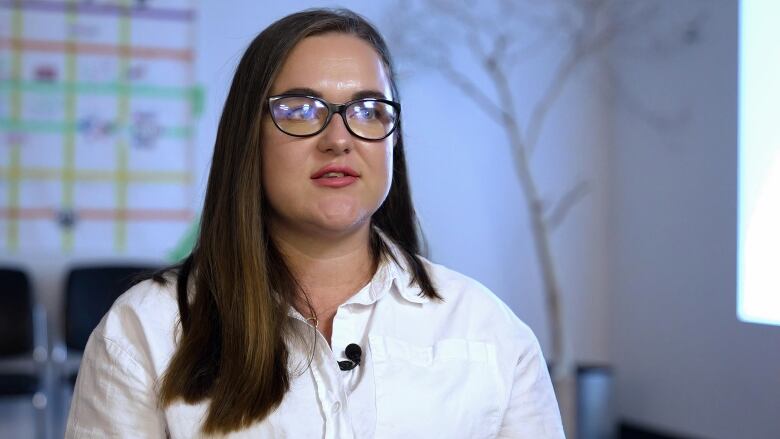 A lady with dark brown hair in a white shirt and thick black glasses.