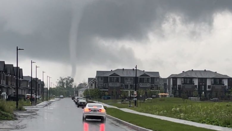 A thin funnel cloud over a suburb in summer.