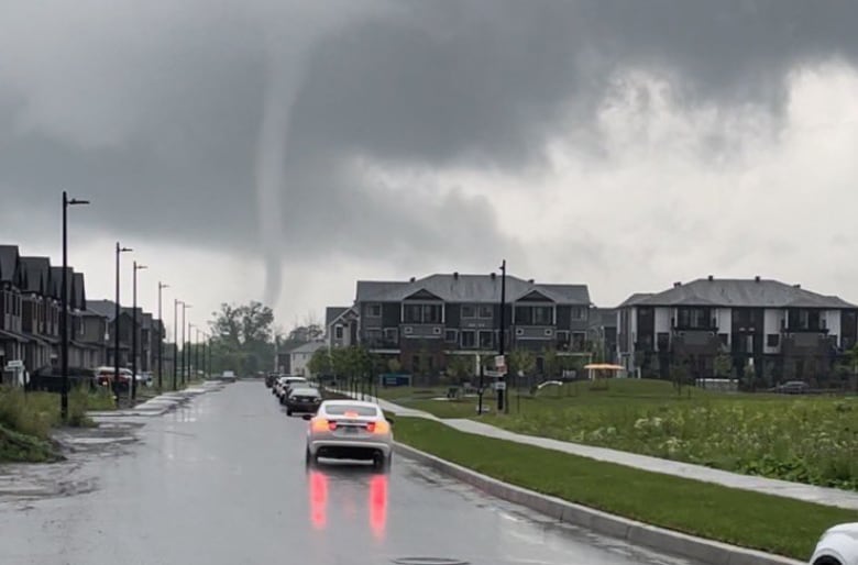 A thin funnel cloud over a suburb in summer.