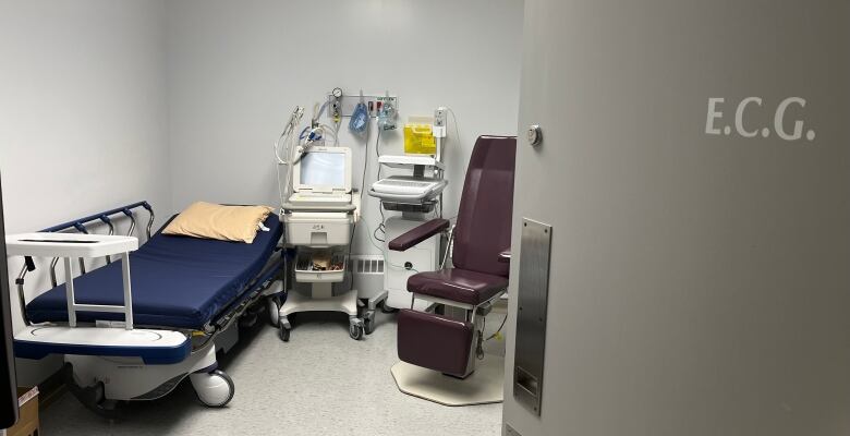 Treatment room in a small hospital, with an empty patient bed and various pieces of medical gear.  