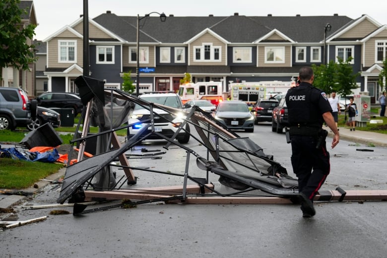 Tangled metal sits on a residential street as a police officer crosses it after a storm.