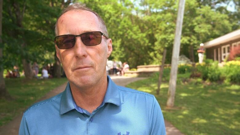 A man in a blue shirt and sunglass looks at the camera.