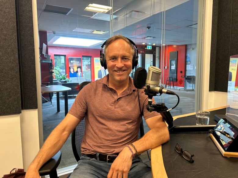 Stuart Hickox in in the CBC radio studio. He's wearing headphone is sitting next to a microphone.