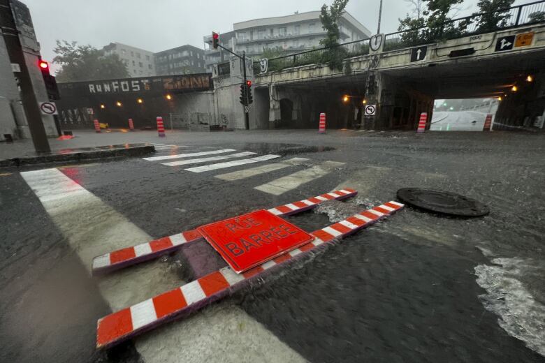 a tumbled over rue barree sign is seen amid flooding near an intersection with several overpasses