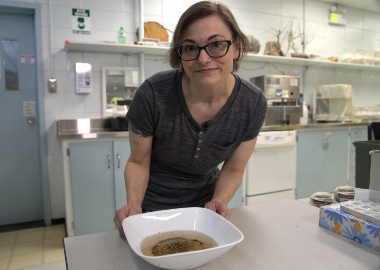 A woman stands over a white bowl full of water and mosquito larvae and pupae inside a lab.