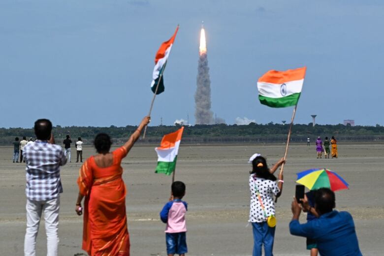 People wave Indian flags as a rocket carrying a spacecraft bound for moon launches.