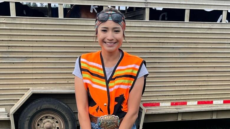 Lita stands in front of a horse trailer wearing her orange competition vest.