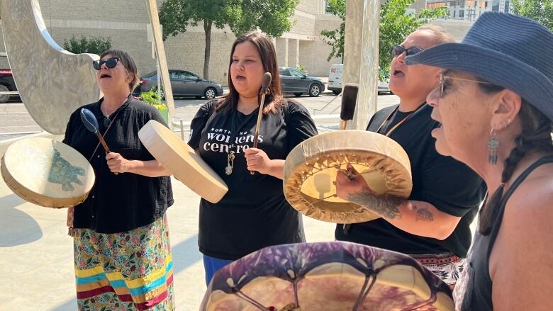 A group of four women sing and drum outside a courthouse. 