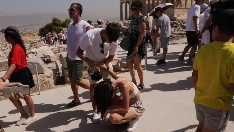 A person is seen bent over while squatting as another holds their hand in support.