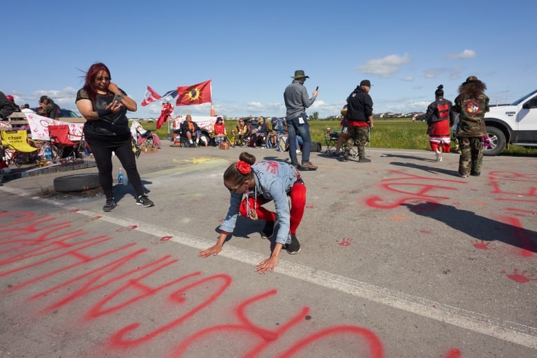 Diane Bousquet, an activists for Indigenous rights, puts red hand prints on the main road into the Brady Road landfill, just outside of Winnipeg, Monday, July 10, 2023, after the city issued an order to vacate the blockade site by Monday at noon. 