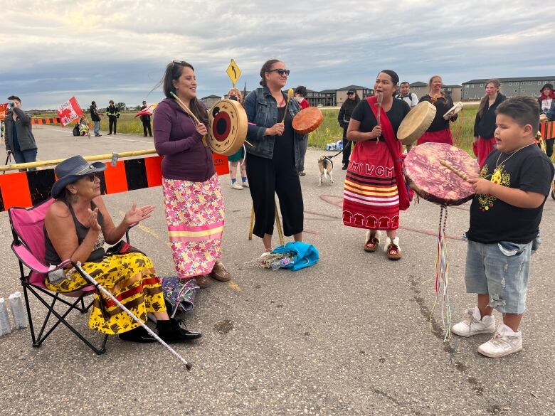 People standing on a road holding drums.